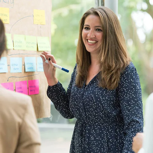 Portret van Claire, teamlid bij Raise. Ze staat voor een prikbord met verschillende kleuren post-its.