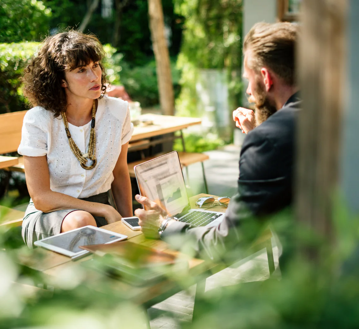 Vrouw en man in overleg aan buitentafel met laptop
